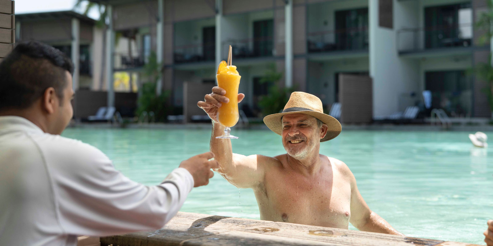 Person toasting the bartender wearing a sun hat while in the pool.