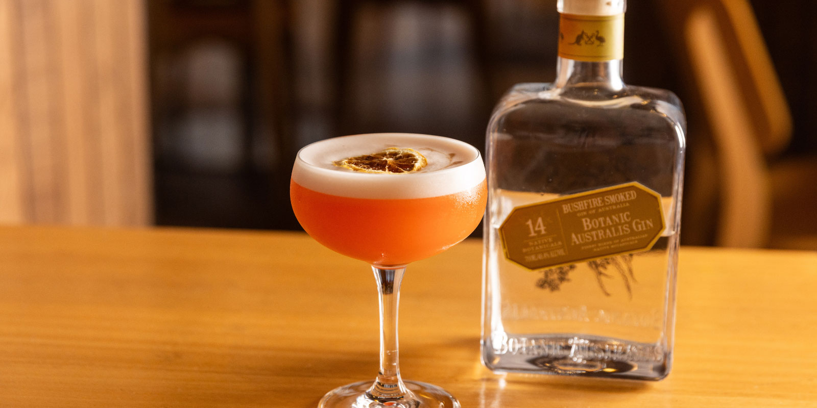 Orange cocktail with a bottle of gin next to it on a wooden table.